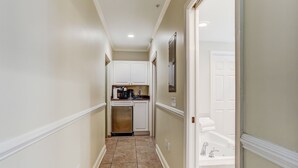 A narrow hallway with a kitchen area at the end, featuring cabinets, a dishwasher, and a sink.