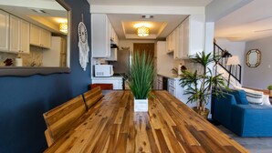 Een moderne keuken met witte kasten, een houten eettafel en een centraal eiland met een plant.