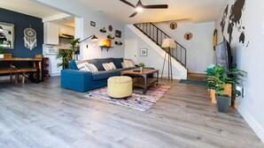 Een moderne woonkamer met een blauwe bank, een houten salontafel en een plafondventilator.