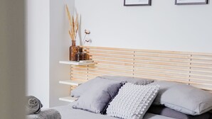 Une chambre à coucher moderne avec une tête de lit en bois, une couvre-lit grise et deux tableaux encadrés accrochés au mur.