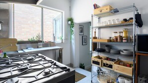 Une cuisine équipée d’une cuisinière à gaz, d’une fenêtre donnant sur un mur en briques et d’une étagère contenant des ustensiles de cuisine et des bocaux.
