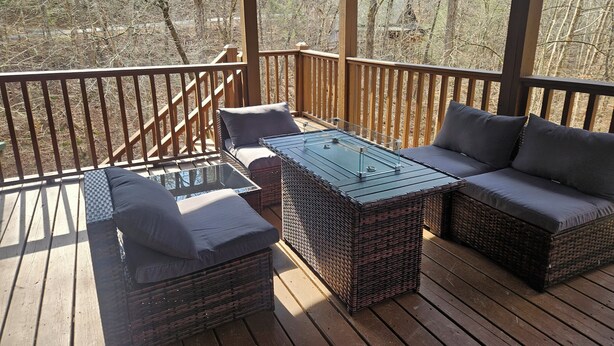 Una terraza techada al aire libre con mobiliario de mimbre, incluyendo un sofá y dos sillones, además de una mesa con cubierta de vidrio.