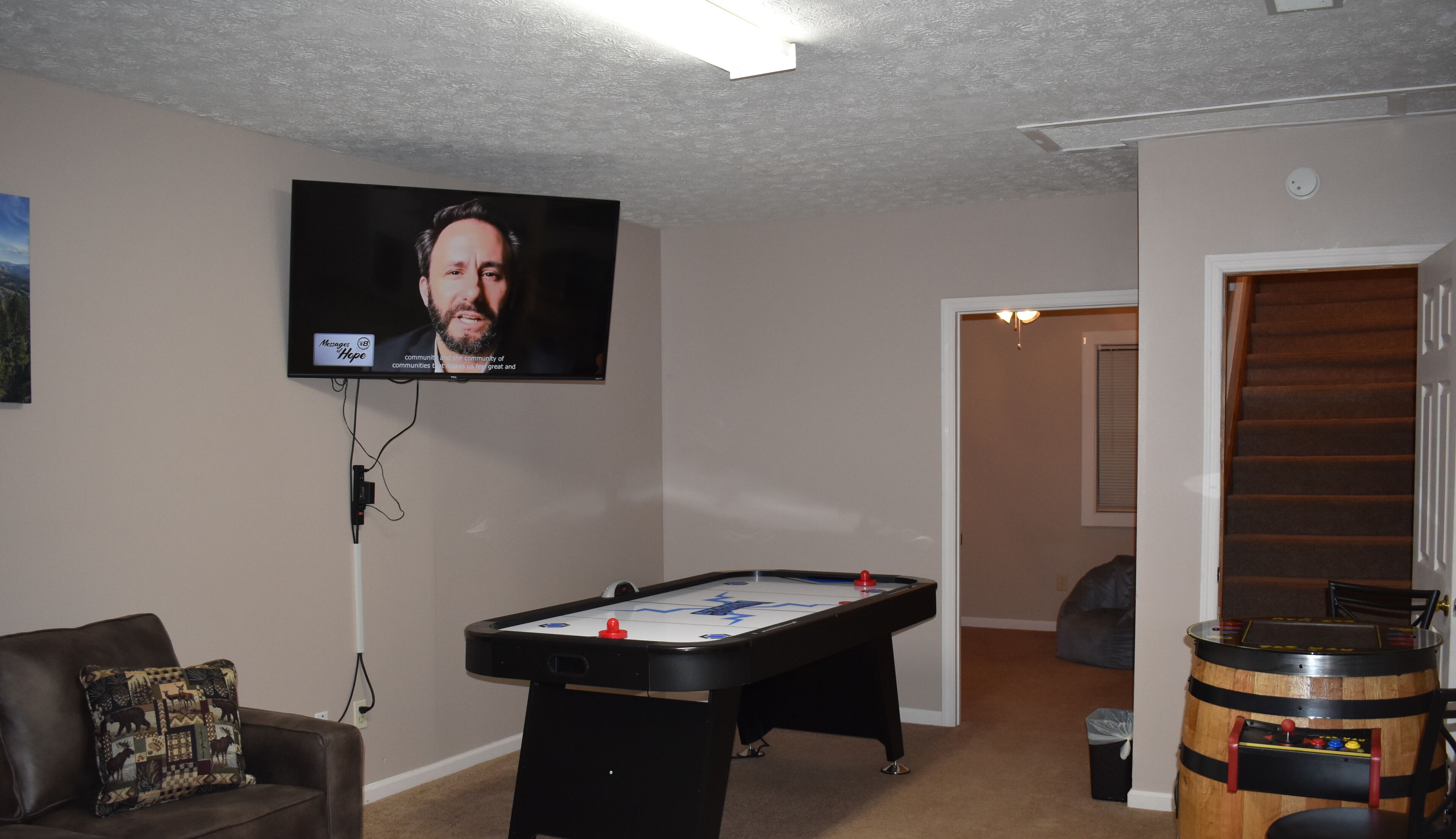 A living room with a pool table, a television mounted on the wall, a couch, and a wooden barrel.