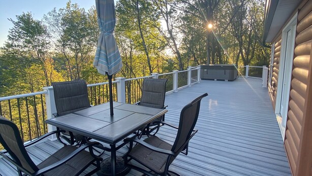Een terras met tafel en stoelen, omringd door een hek, met uitzicht op een bebost gebied.