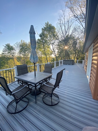 A deck with a table and chairs, surrounded by a railing, overlooking a forested area.