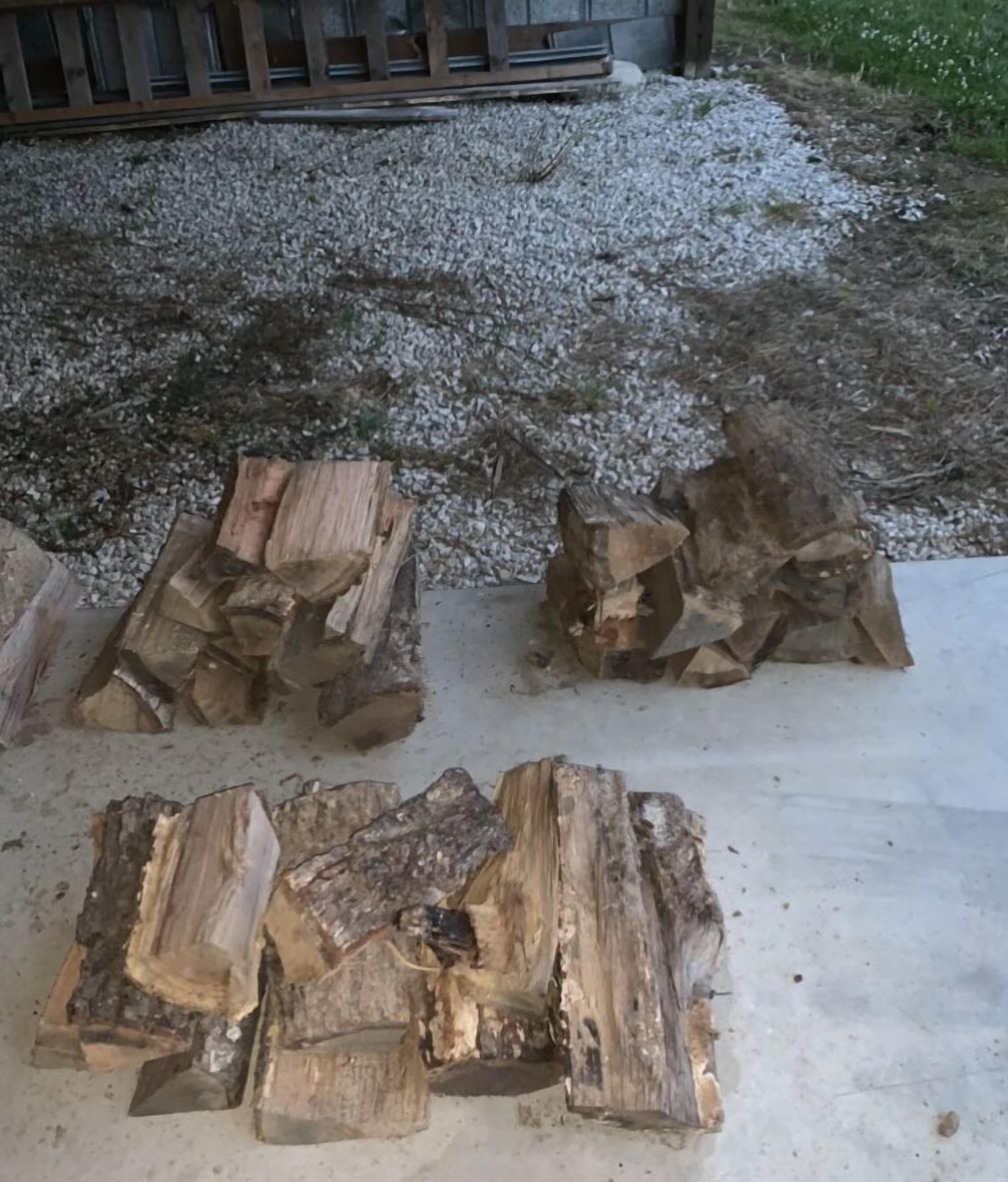 Een stapel hout buiten, met een grindpad en een houten hek op de achtergrond.
