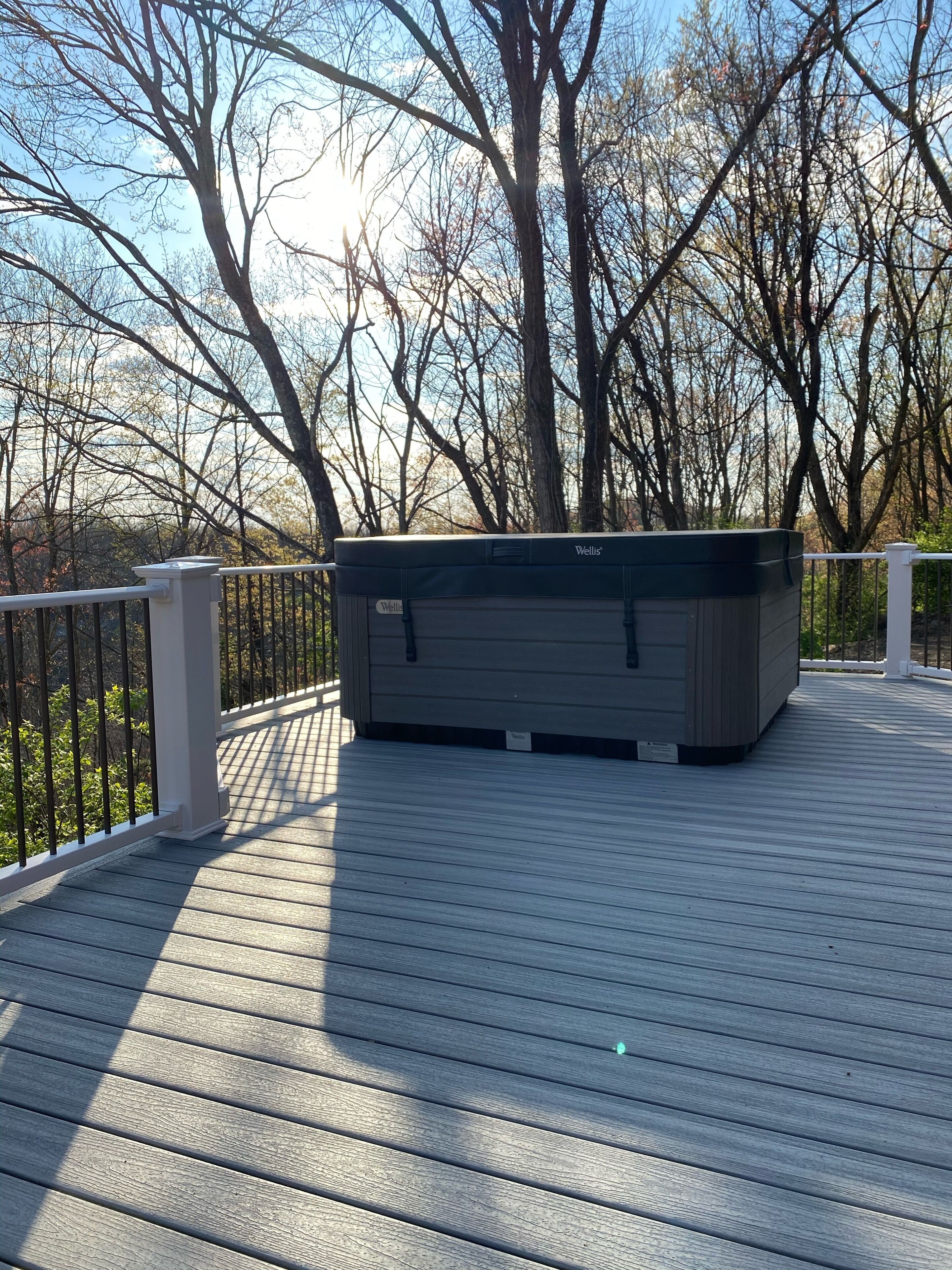 A wooden deck with a built-in hot tub, surrounded by a white railing and trees in the background.