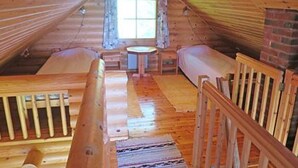 Een gezellig chalet met een slaapkamer op de zolder, houten wanden, een kleine eethoek en een open haard.