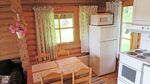 Een knus kamer in chaletstijl met houten inrichting, een eettafel met stoelen, een koelkast, een kookplaat en een raam met gordijnen.