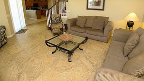 A living room with a sofa, armchair, and coffee table. There is a staircase leading to another room. - Overlooking the golf course with spacious interior! (Davenport)