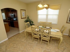 A dining area with a table set for four, surrounded by wooden chairs, a potted plant, and a window with blinds.