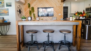 A bar area with a wooden herringbone wall, a flat-screen TV, and three stools. - Belmont Shore BH - Unit A  (Long Beach)