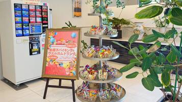 A vending machine with multiple screens, a framed sign with Japanese text, and a tiered display of snacks.