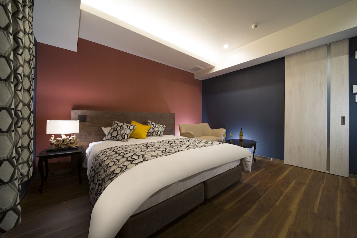 A modern hotel room with a large bed, a nightstand with a lamp, and a wardrobe.