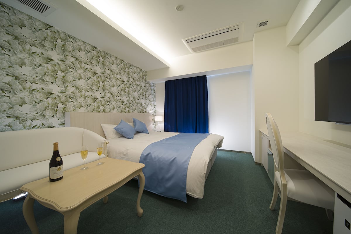 A hotel room with a bed, a desk, a bottle of wine, and two glasses of wine on the desk.