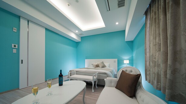 Ein modernes Schlafzimmer mit einem Bett, einem weißen Sofa, einem kleinen Tisch mit Weingläsern und einer Weinflasche.
