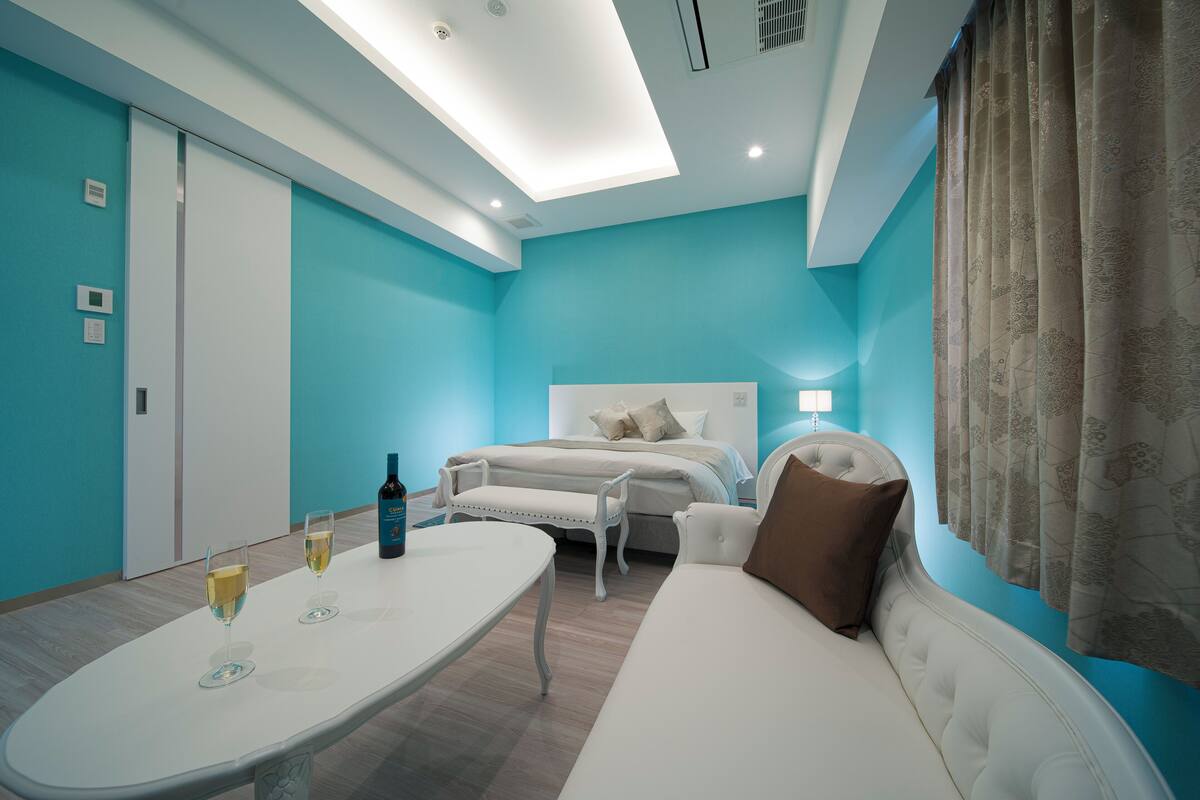 A modern bedroom with a bed, a white sofa, a small table with glasses of wine, and a bottle of wine.
