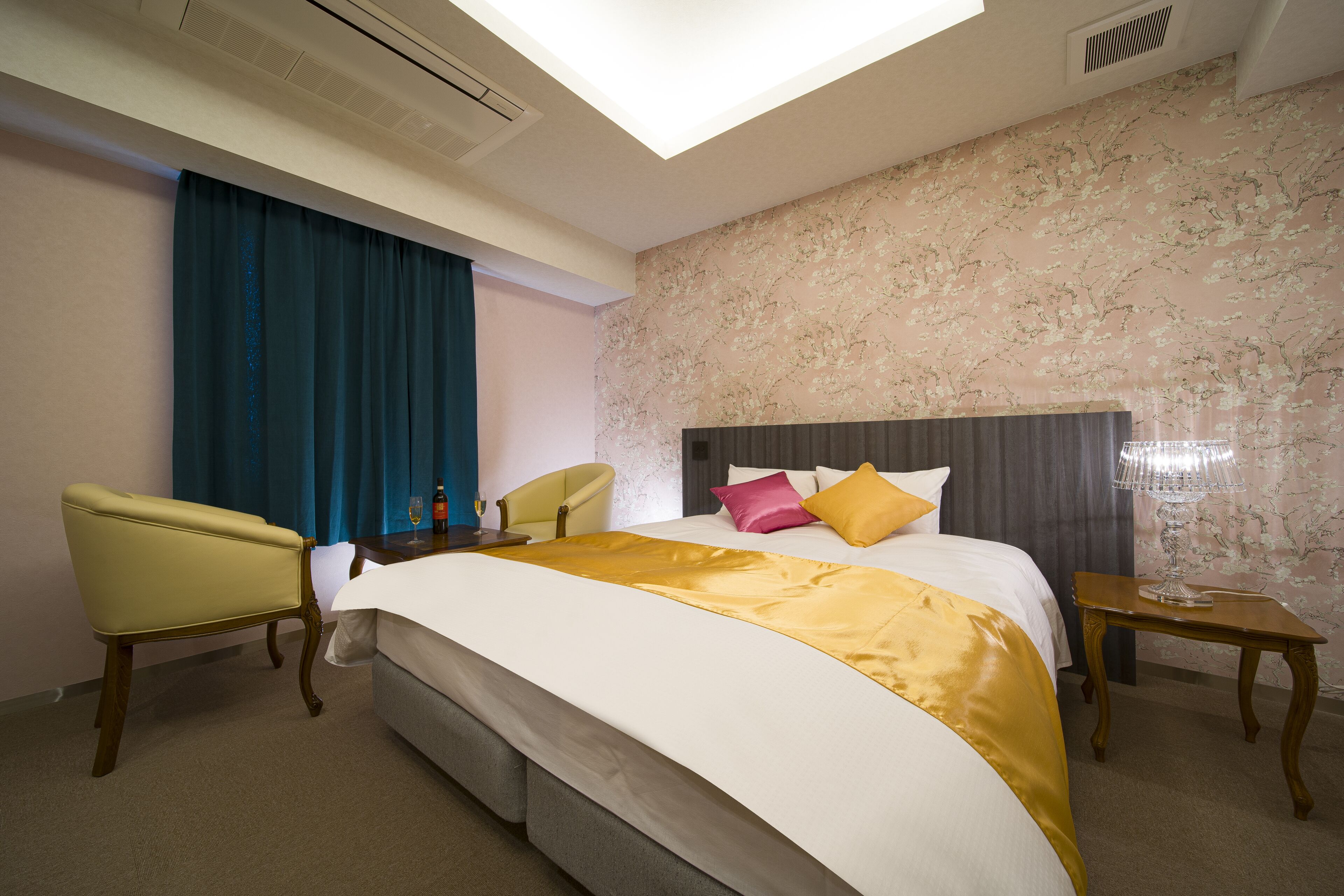 A hotel room with a large bed, a chair, a nightstand, and a window with curtains.
