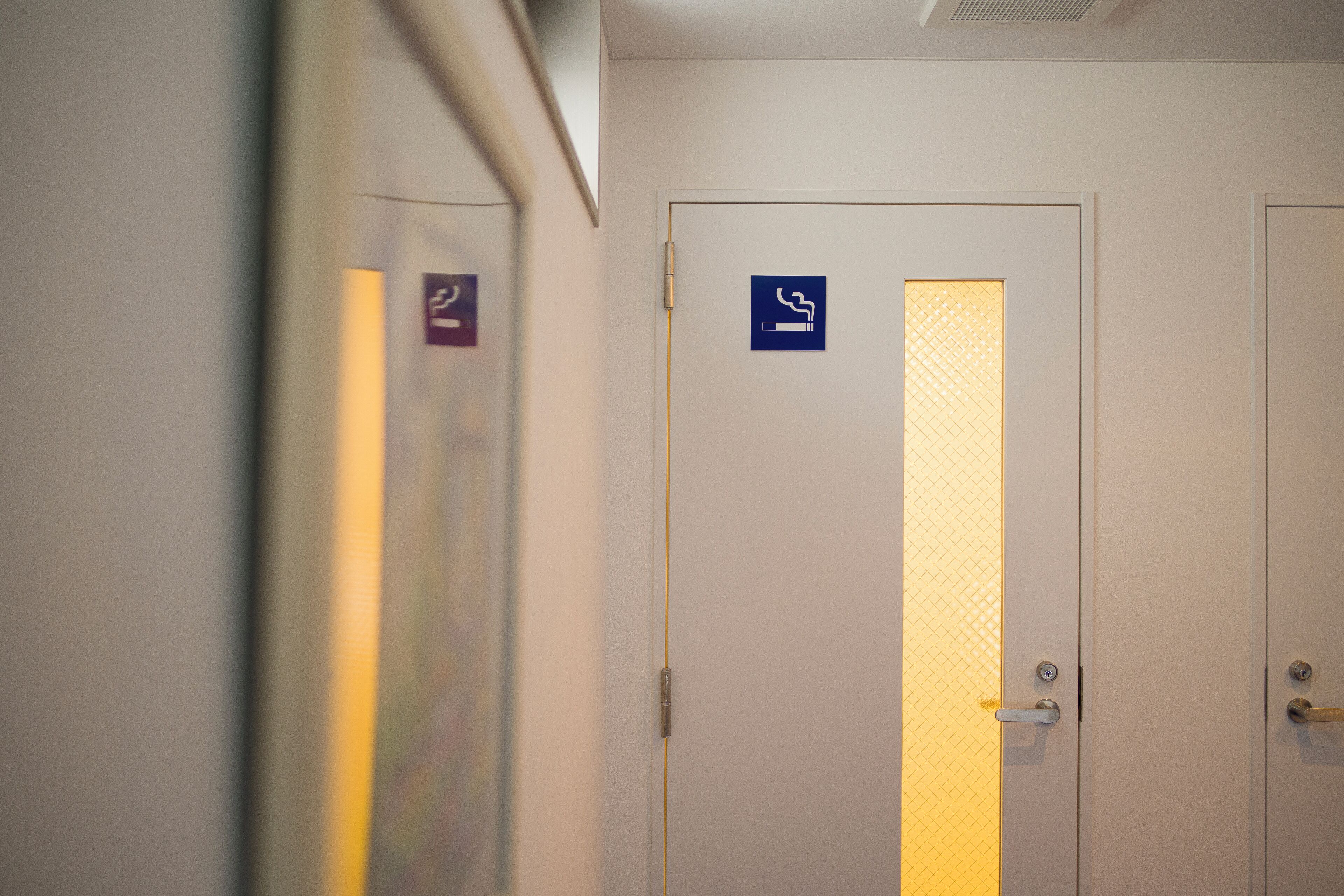Un couloir avec des portes, dont l’une est ornée d’un panneau indiquant qu’il est interdit de fumer.