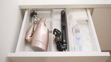 A drawer containing a hair dryer, a black charging cable, and a set of white bottles.