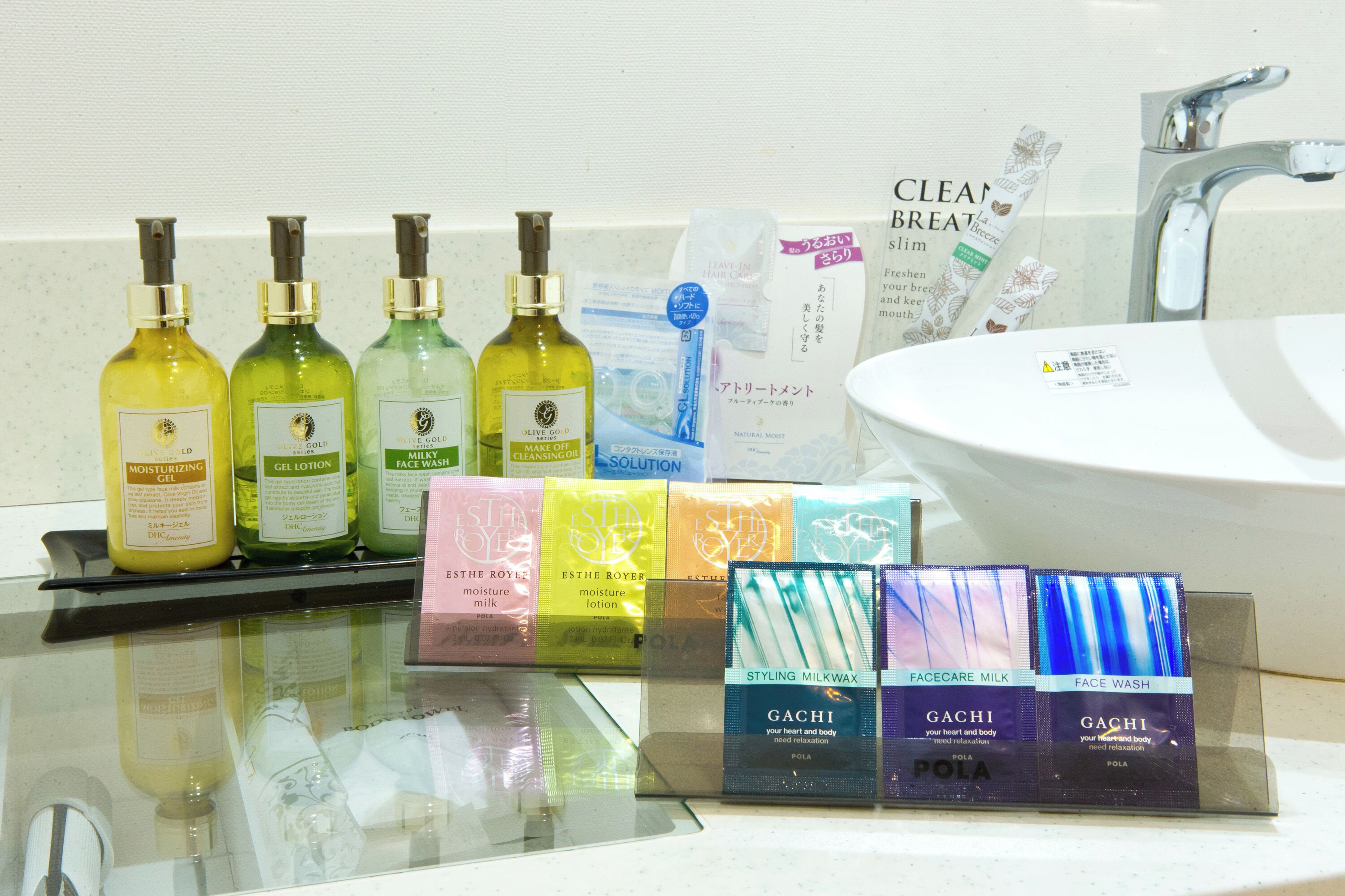 A bathroom with a sink, mirror, and various toiletries including lotions, creams, and a face wash.