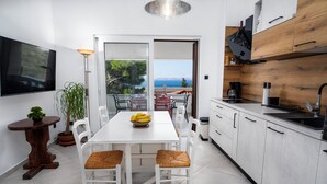 Una cocina moderna con armarios blancos, una mesa de comedor con sillas de mimbre, una planta en maceta y vistas al mar a través de un ventanal.