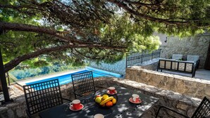 Una mesa dispuesta con tazas y un frutero, con vista a una piscina y un muro de piedra.