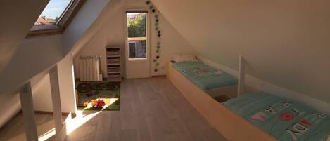 A small attic bedroom with two beds, a skylight, and a view of the outside.
