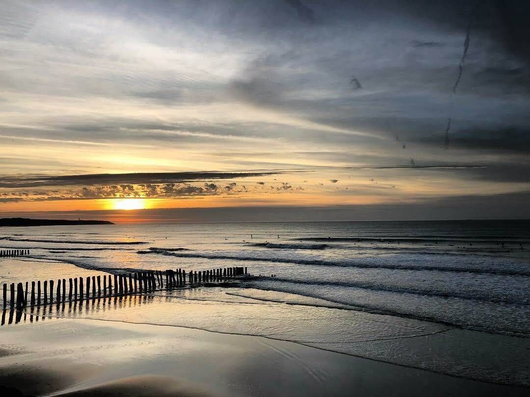 Ein Strandbild mit Sonnenuntergang, Wellen und einem Holzzaun.