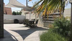 Een terras buiten met een houten terras, een tafel met stoelen en een grote parasol voor schaduw.