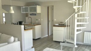 Een moderne keuken met witte kasten, een eethoek met een houten tafel, en een witte trap.