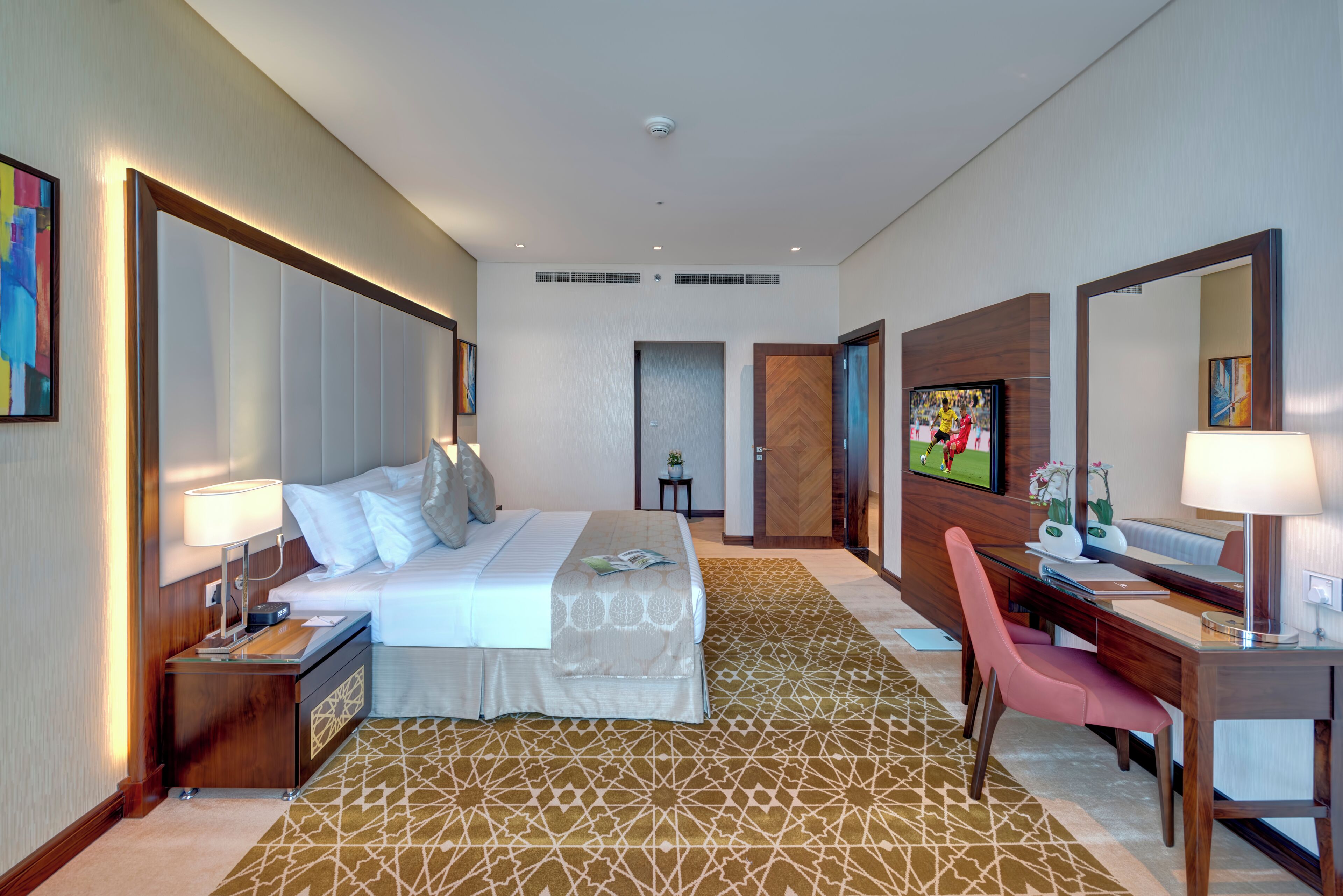 A hotel room with a bed, bedside table, desk, chair, and a large mirror.