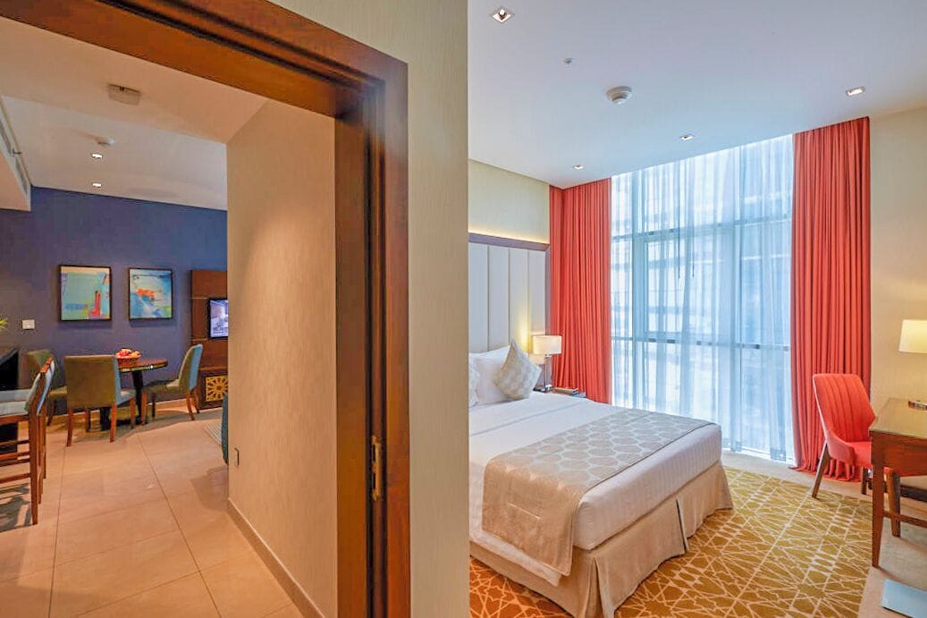 A hotel room with a bed, a desk, a chair, a TV, and artwork on the wall.