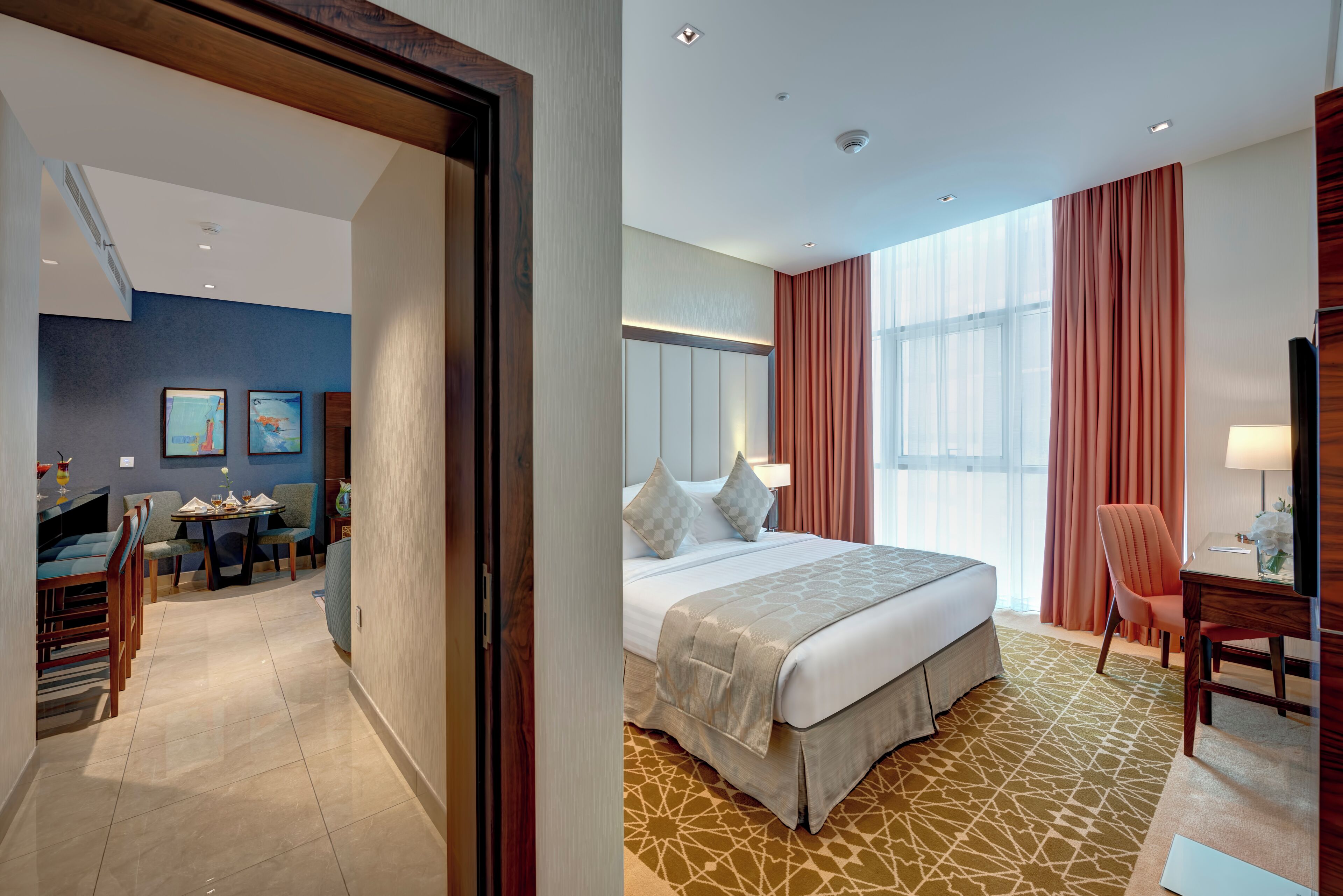 A hotel room with a bed, a desk, a chair, and a dining area with chairs and a table.