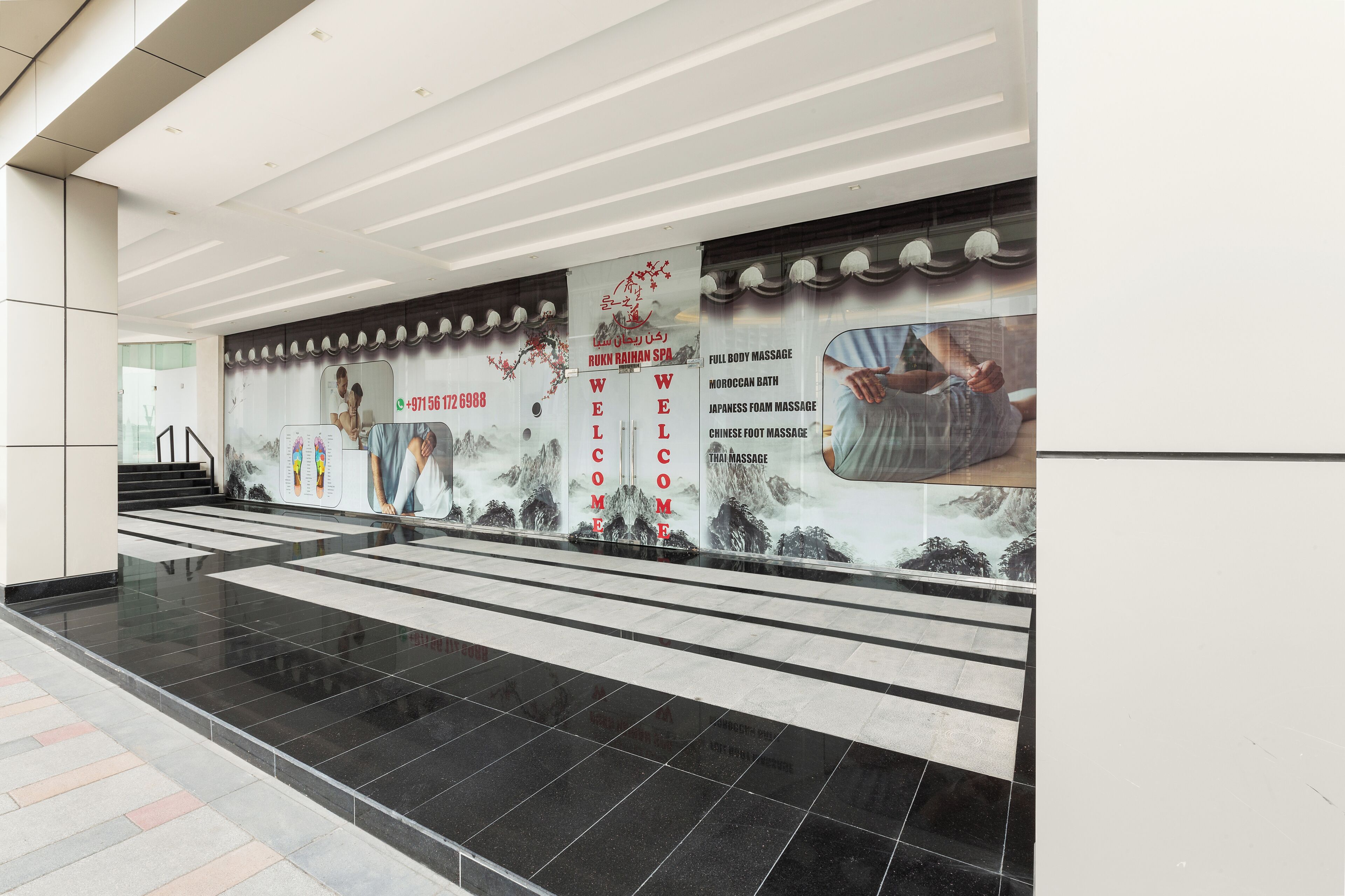 A modern interior with a tiled floor, a staircase, and a wall with a welcome sign and massage services advertisement.