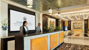 En hotellobby med modern design, med en receptionsdisk, en stor digital skärm som visar hotellets namn och ett dekorativt tak.