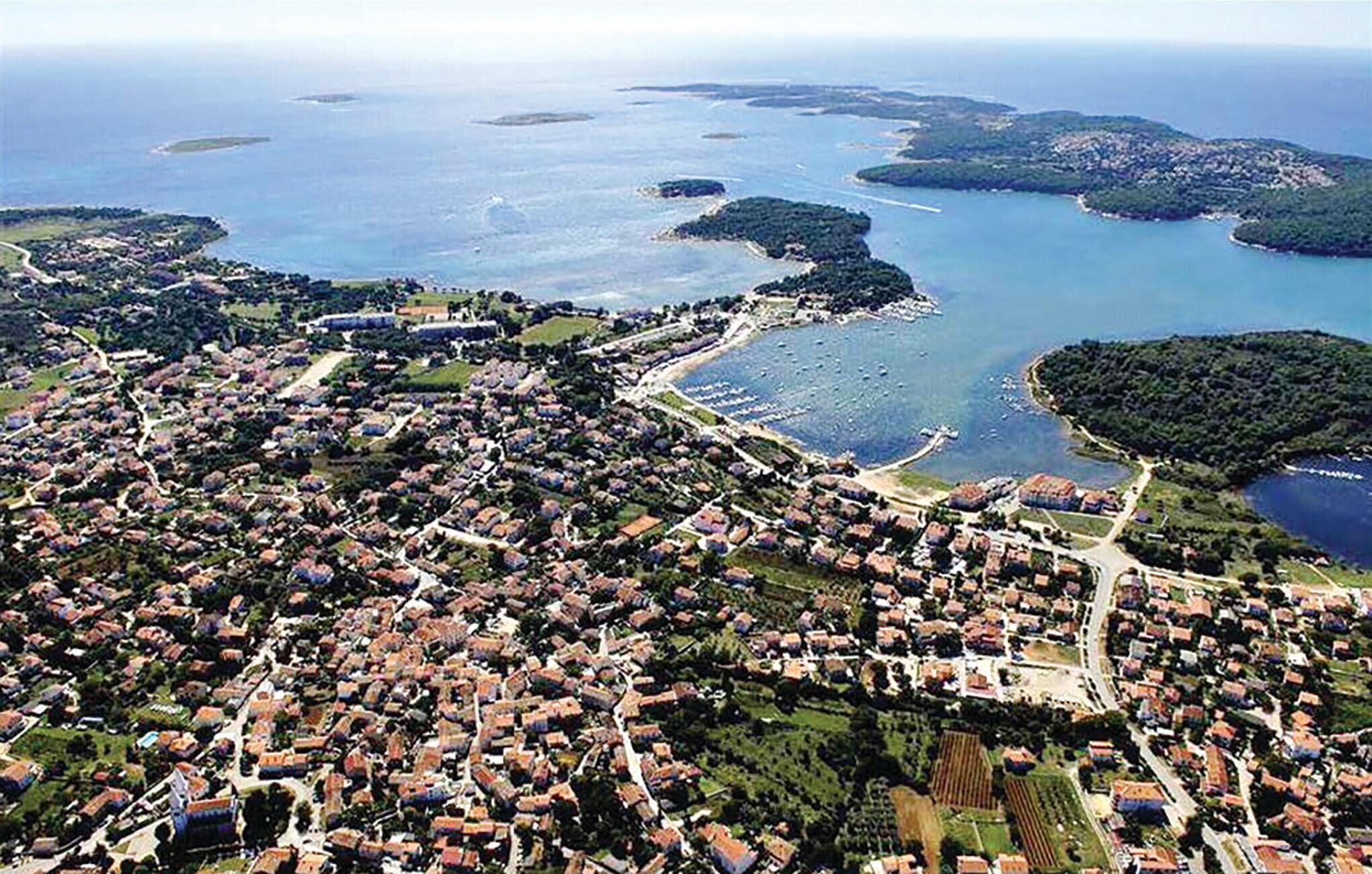 Vue aérienne d’une ville côtière avec des habitations densément regroupées, une route principale et un port de plaisance.