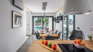 A modern dining area with a wooden table, chairs, and a view of a swimming pool. - Beach front home in Medulin (Medulin)