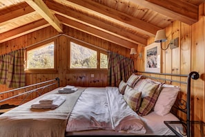 A wooden cabin bedroom with a bed, a nightstand, a lamp, and a window with curtains.