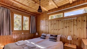 A wooden cabin bedroom with a bed, two bedside tables, and a window with curtains. - Chalet Khione - La Tzoumaz, 4 Vallees (La Tzoumaz)
