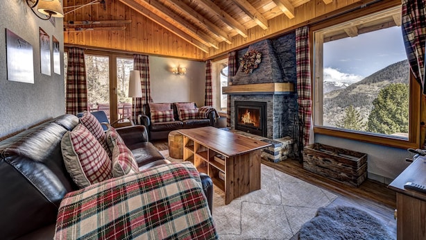 A cozy living room with a fireplace, wooden ceiling beams, and a large window offering a mountain view. - Chalet Khione - La Tzoumaz, 4 Vallees (La Tzoumaz)