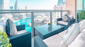 A balcony with wicker furniture, a glass table, and a view of a cityscape and water. - Elite Royal Apartment - Burj Khalifa & Fountain view - Grand (Dubai)