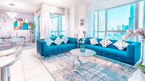 A modern living room with a blue sofa, a glass coffee table, and large windows offering a city view. - Elite Royal Apartment - Burj Khalifa & Fountain view - Grand (Dubai)
