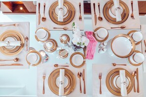 Une table dressée pour quatre personnes, avec de la vaisselle dorée et blanche, comprenant des assiettes, des bols et des tasses.