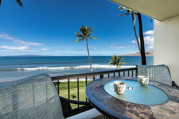 Un balcon avec une table et des chaises donnant sur l’océan, offrant une vue sur la mer et les palmiers.