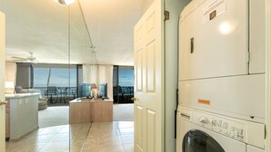 Une buanderie équipée d’un lave-linge à chargement frontal, d’un petit coin cuisine et donnant sur le balcon.