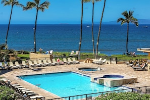 A pool area with lounge chairs and a hot tub, overlooking the ocean.