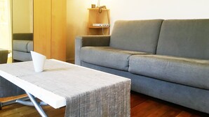 A living room with a grey sofa, a small table with a white object on it, and a wooden cabinet with a lamp. - Monceau (Claude Pouillet) ID 302 (Paris)