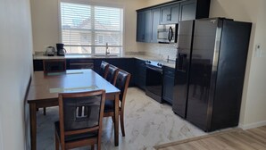 Una cocina moderna con armarios oscuros, un refrigerador de acero inoxidable, microondas integrado y un comedor con mesa y sillas de madera.