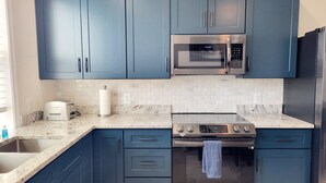 Una cocina con armarios azules, un microondas de acero inoxidable, un horno empotrado y un lavamanos.